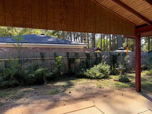 Covered patio featuring a wood-plank ceiling, concrete flooring, and support post, opening to a fenced backyard with established landscaping