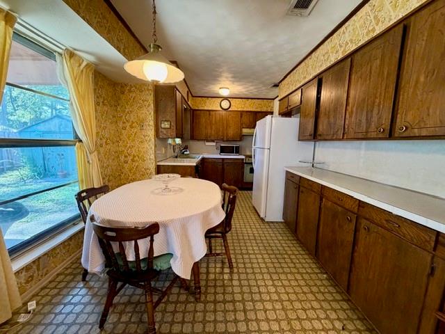 Kitchen featuring wood cabinetry, extensive countertop surface, pendant lighting, and a large window