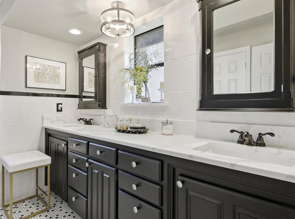 Double vanity featuring black cabinetry, light-toned stone-finish countertops with integrated dual sinks, dark metallic hardware, and matching wall-mounted mirrored medicine cabinets