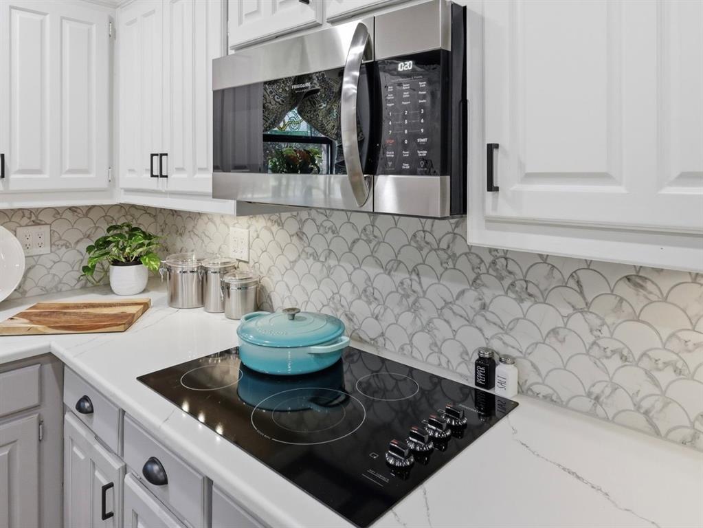 Kitchen area featuring white shaker-style cabinetry with matte black hardware, integrated stainless steel microwave, black glass cooktop, and patterned scalloped backsplash tiling