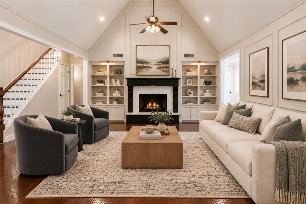 Living area featuring a vaulted ceiling with panel molding, built-in floor-to-ceiling shelving, a fireplace with a decorative mantle, and wood-finish flooring