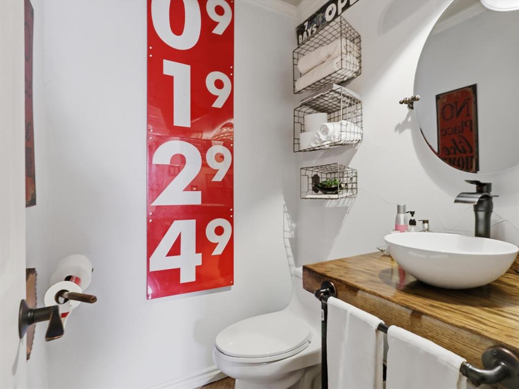 Custom wood-slab countertop with a white vessel sink, matte black faucet, wall-mounted wire storage baskets, and a circular mirror