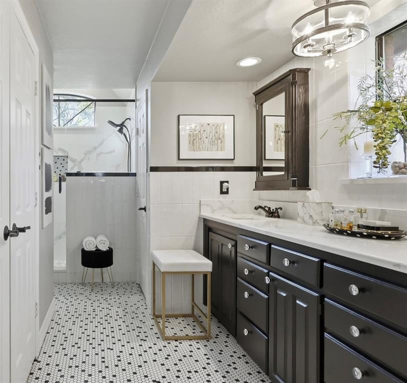 Bathroom featuring a black vanity with a light-toned countertop, custom tile flooring, a wall-mounted dark wood medicine cabinet, and a walk-in shower with tile surround