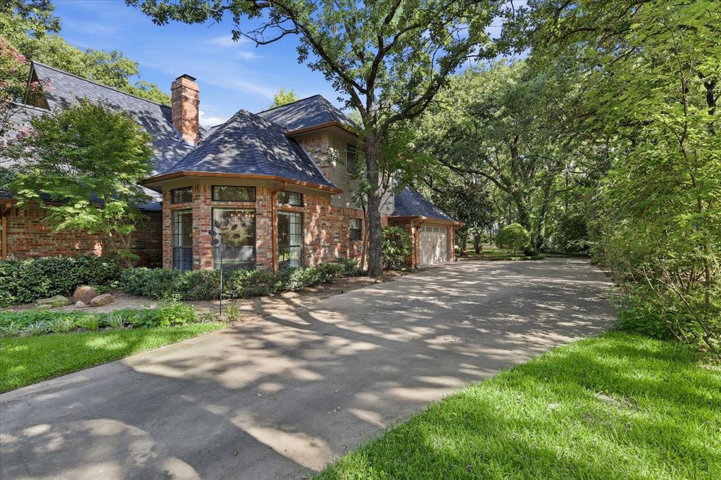 Brick exterior featuring a multi-gabled roofline, brick chimney, large driveway, and mature landscaping