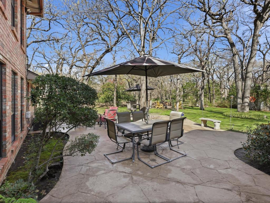 Flagstone-patterned concrete patio featuring brick exterior wall, mature hardwood trees, and manicured lawn
