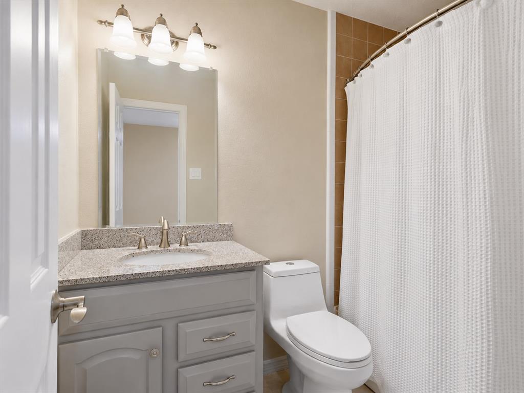 Bathroom featuring a grey vanity with stone-finish countertop, undermount sink, brushed nickel hardware, three-light fixture, and a curved shower rod