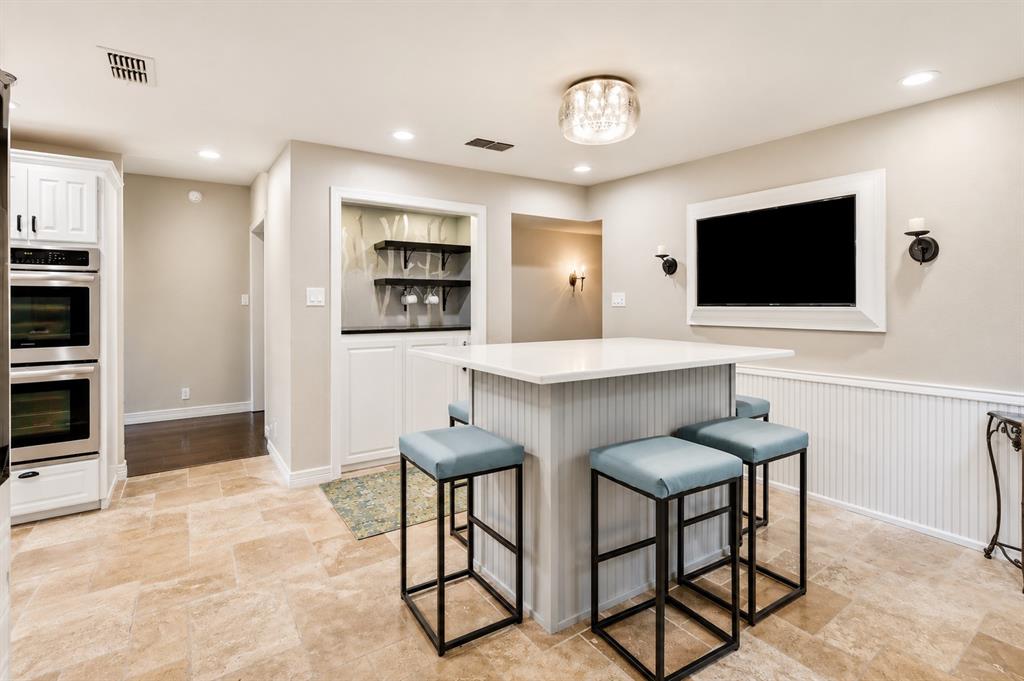 Kitchen featuring stone flooring, a center island with a white countertop, built-in double ovens, recessed wall-mounted shelving with cabinetry, and beadboard wall paneling