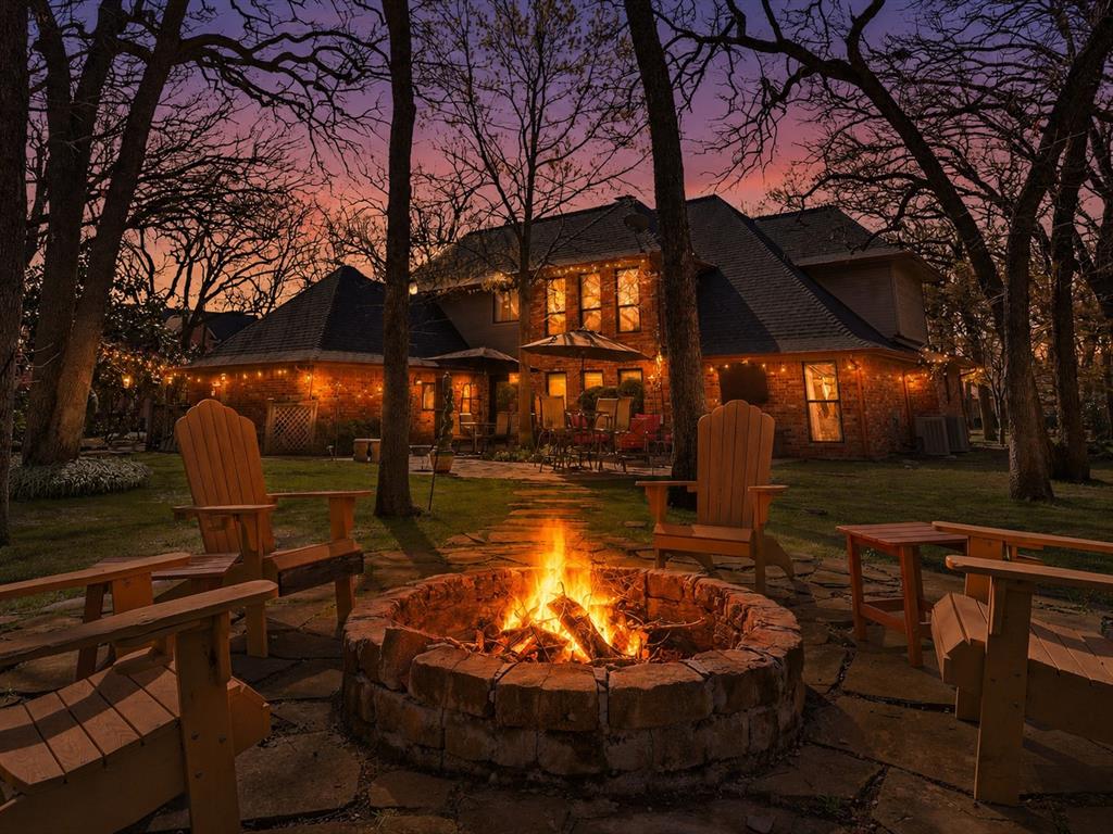 Backyard featuring a stone-encased fire pit, flagstone patio, brick exterior, and mature trees