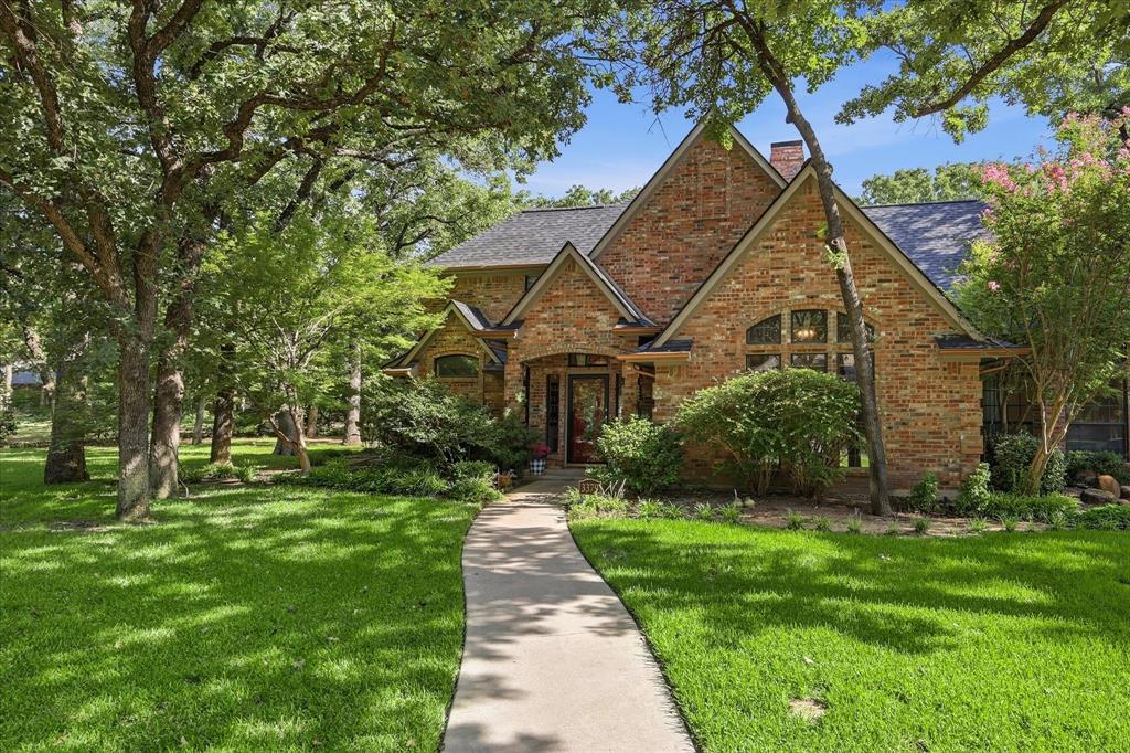 Multi-gabled brick exterior featuring a covered entryway, arched windows, and a paved walkway, surrounded by mature trees