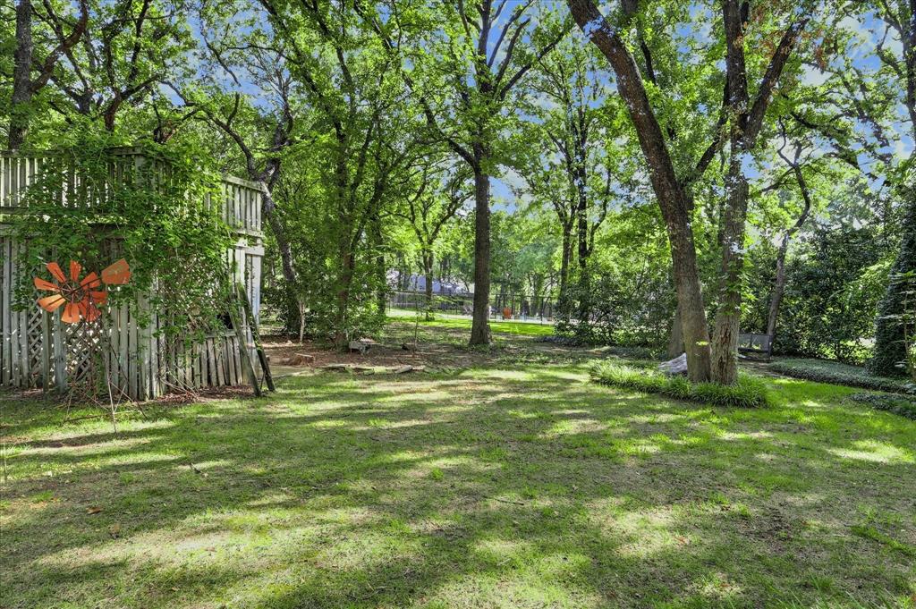 Expansive backyard featuring mature shade trees, a grass lawn, decorative metal windmill, and tiered wooden fencing