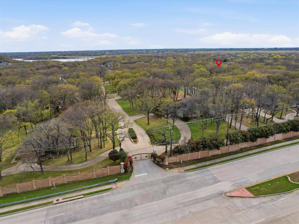 Aerial perspective of a gated entrance with brick perimeter wall, concrete driveway, and mature landscaping