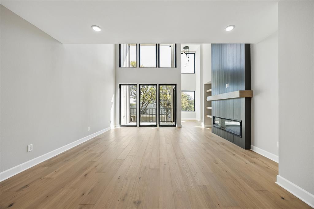 Double-height ceiling, floor-to-ceiling windows, wood-finish flooring, recessed lighting, and a floor-to-ceiling fireplace surround with built-in shelving