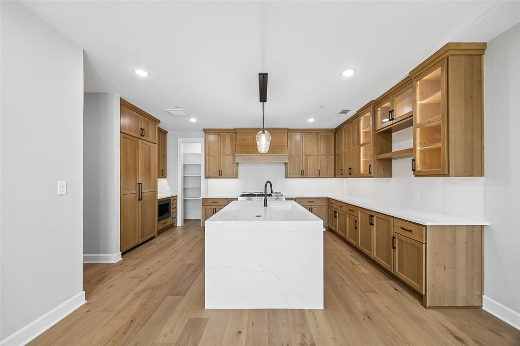 Kitchen featuring shaker-style cabinetry with integrated panel-ready appliances, a central quartz-topped island, wood-finish flooring, recessed lighting, and a walk-in pantry
