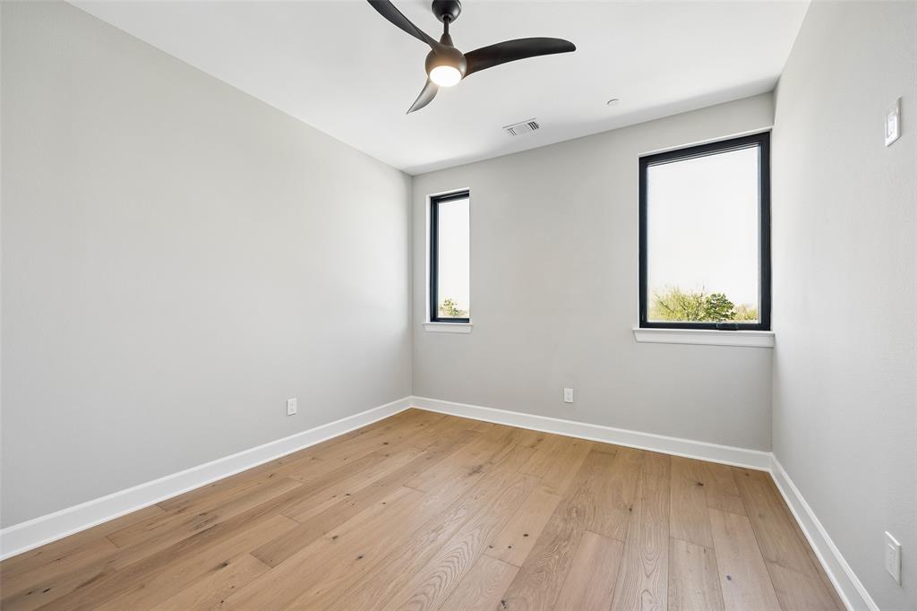 Interior space featuring wood-finish flooring, neutral walls, two windows with black frames, and a ceiling-mounted light fixture with a fan
