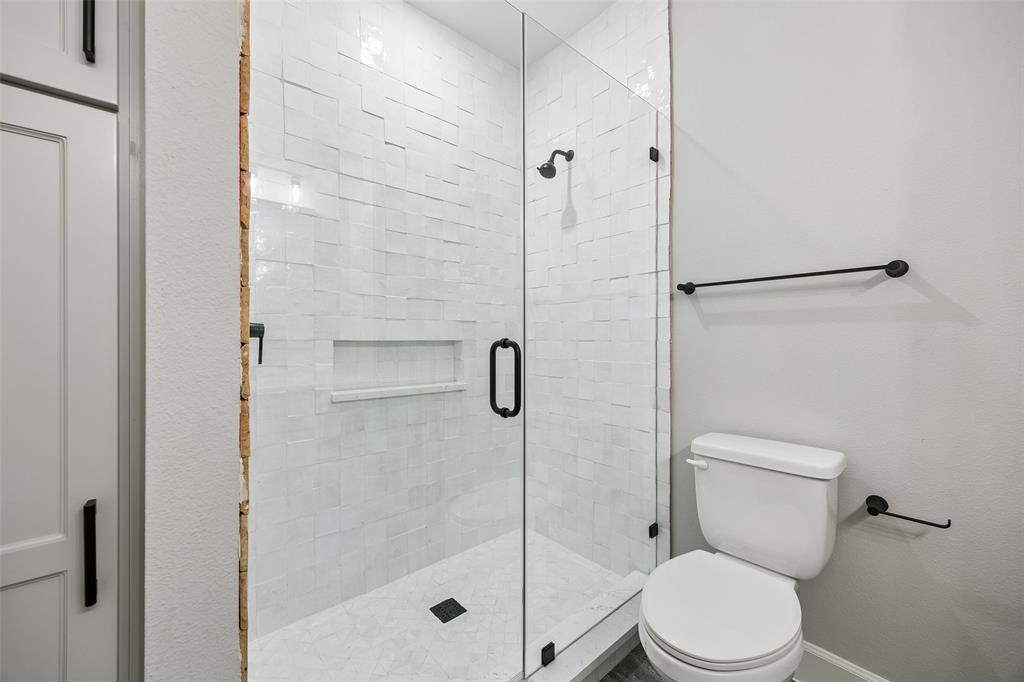 Walk-in shower featuring textured white tile walls, built-in recessed niche, frameless glass door, and matte black fixtures, paired with a coordinating toilet and matte black hardware