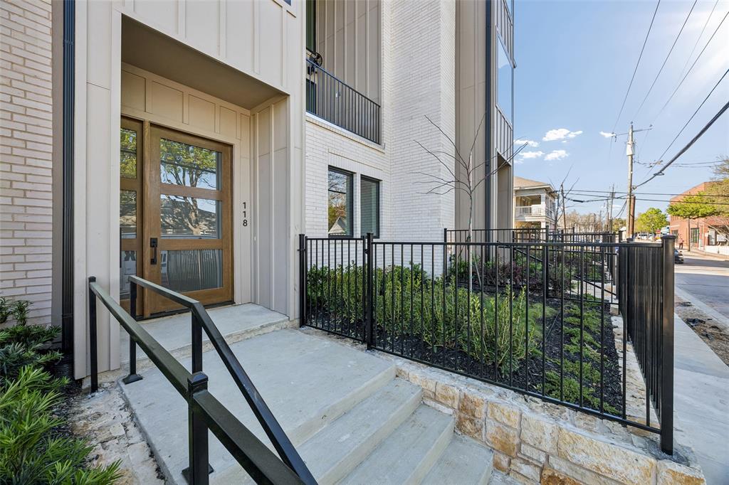 Modern exterior featuring a wood-panel door with glass inserts, vertical siding, painted brick facade, concrete entry steps, and a stone-base perimeter fence