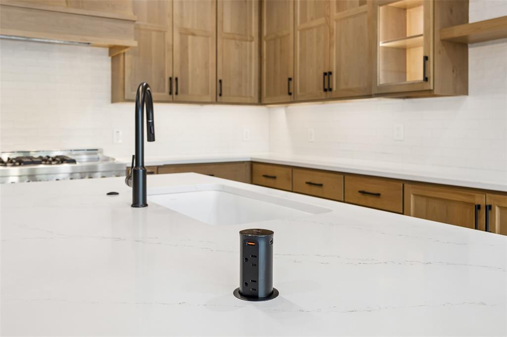 Kitchen island featuring stone countertops, an undermount sink with a matte black high-arc faucet, and a pop-up electrical outlet, complemented by shaker-style cabinetry and a tiled backsplash