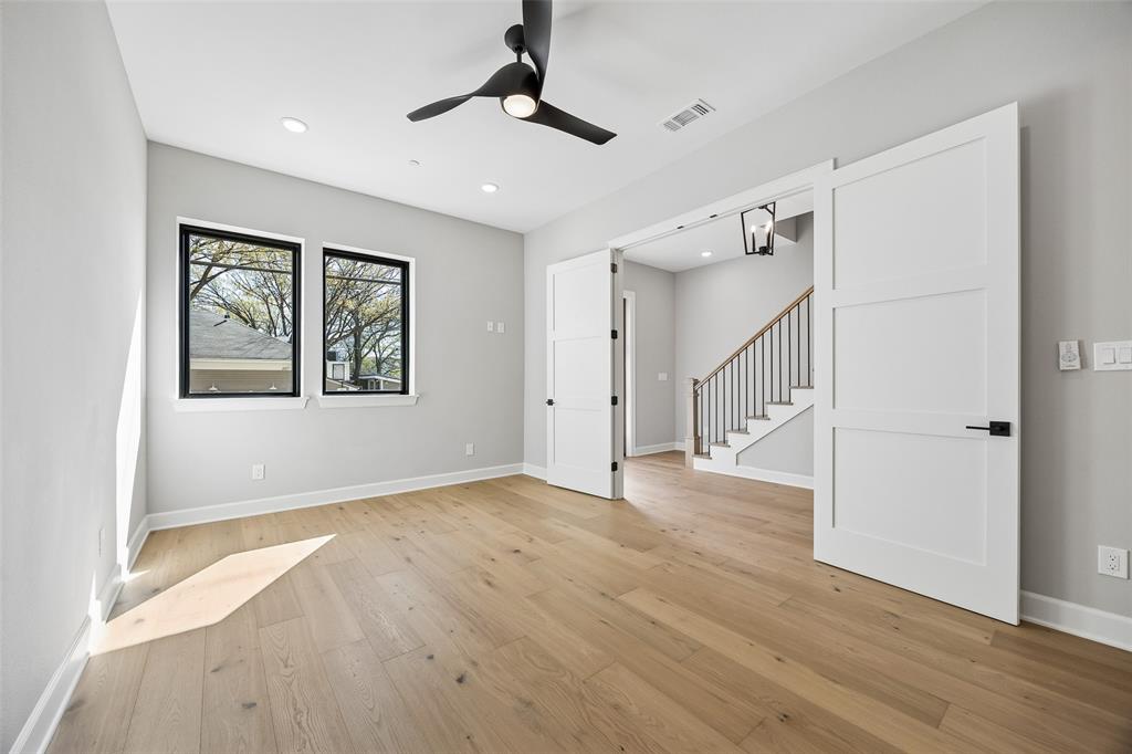 Light-filled interior featuring wood-finish flooring, dual sliding barn-style doors, matte black window frames, and a modern ceiling fan
