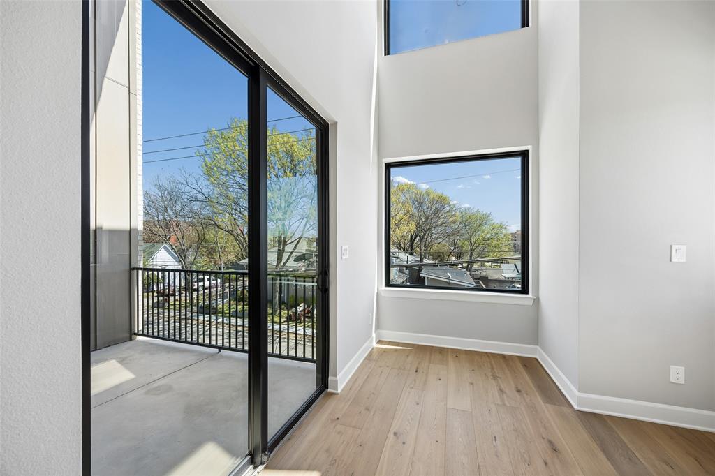Double-height ceiling, floor-to-ceiling sliding glass doors, wood-finish flooring, metal-railed balcony, and expansive window placements