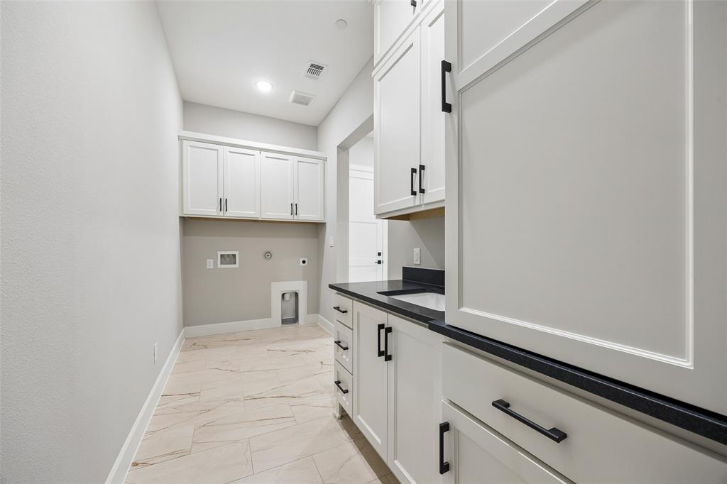 Laundry room featuring white cabinetry, dark countertops, integrated sink, and large-format tile flooring with matte black hardware