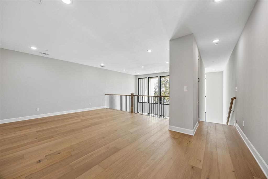 Open interior space featuring wood-finish flooring, recessed lighting, multi-pane windows with dark frames, and metal baluster railing