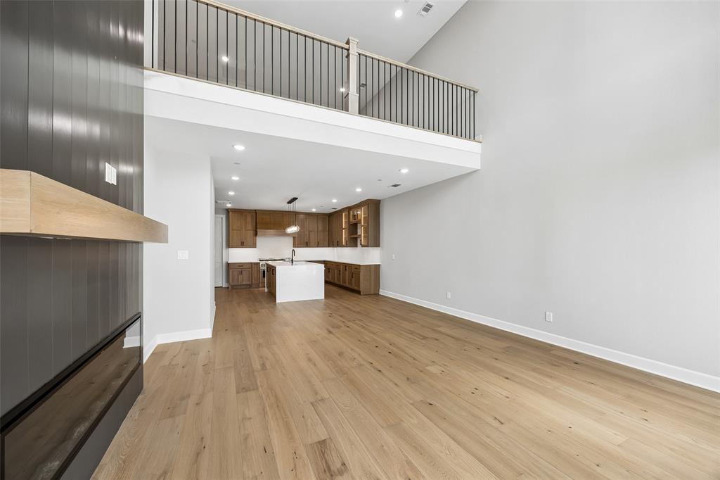 Vaulted ceilings featuring a mezzanine level with a metal spindle railing, wood-finish flooring, a linear fireplace with a natural wood mantle, and a kitchen with a center island