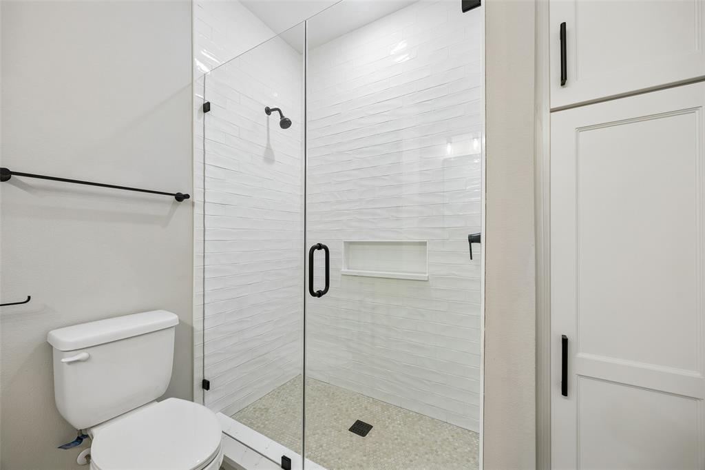 Walk-in shower featuring a frameless glass door, textured wall tile, integrated storage niche, and matte black hardware, accompanied by floor-to-ceiling built-in cabinetry