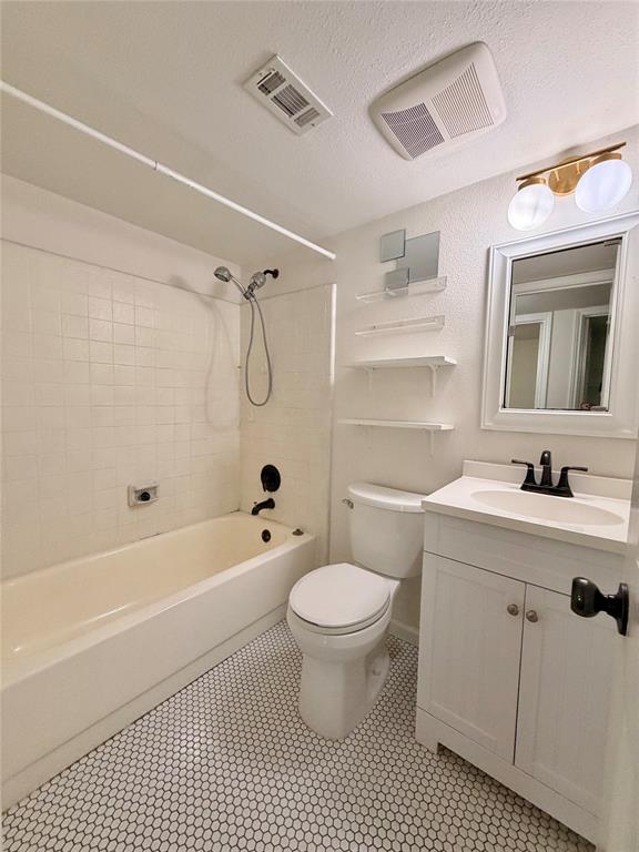 Bathroom featuring a white vanity cabinet with a stone-top integrated sink, black dual-handle faucet, white tile shower surround with a handheld shower head, and small-format hexagonal floor tiling