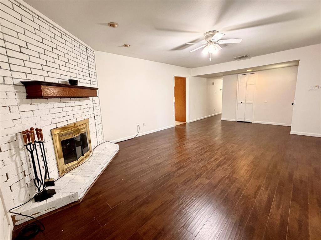Living area featuring white-painted brick fireplace with a wood mantel, wood-finish flooring, and a ceiling fan