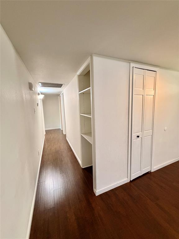 Hallway featuring wood-finish flooring, built-in shelving, and a white bifold closet door