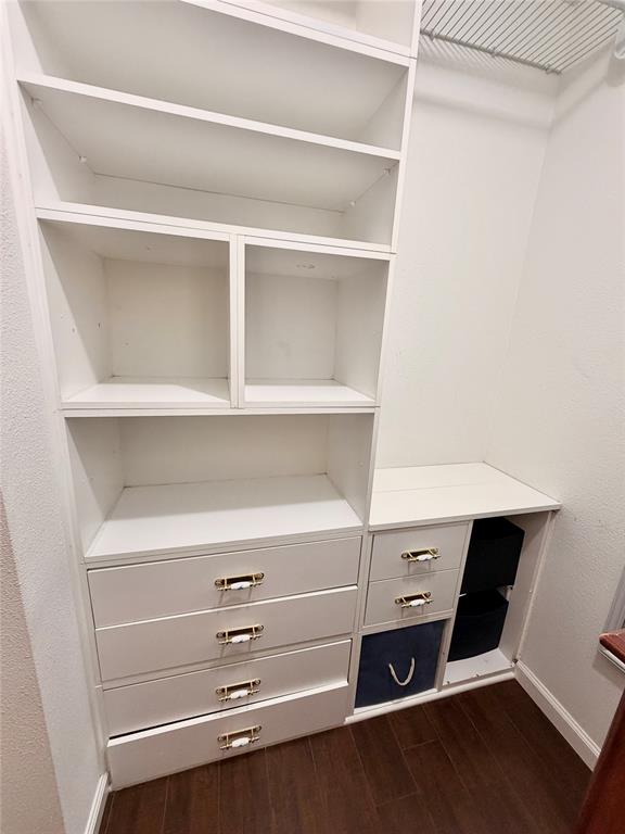 Custom white built-in shelving featuring four deep drawers, two open cubbies, and an integrated wire rack for overhead storage, finished with metallic hardware and wood-finish flooring
