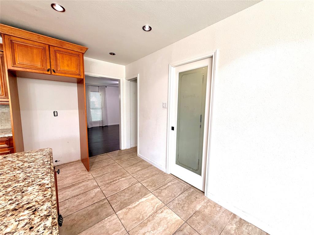 Natural stone countertops, wood-finish cabinetry, recessed lighting, and a door with a frosted glass pane featuring decorative trim