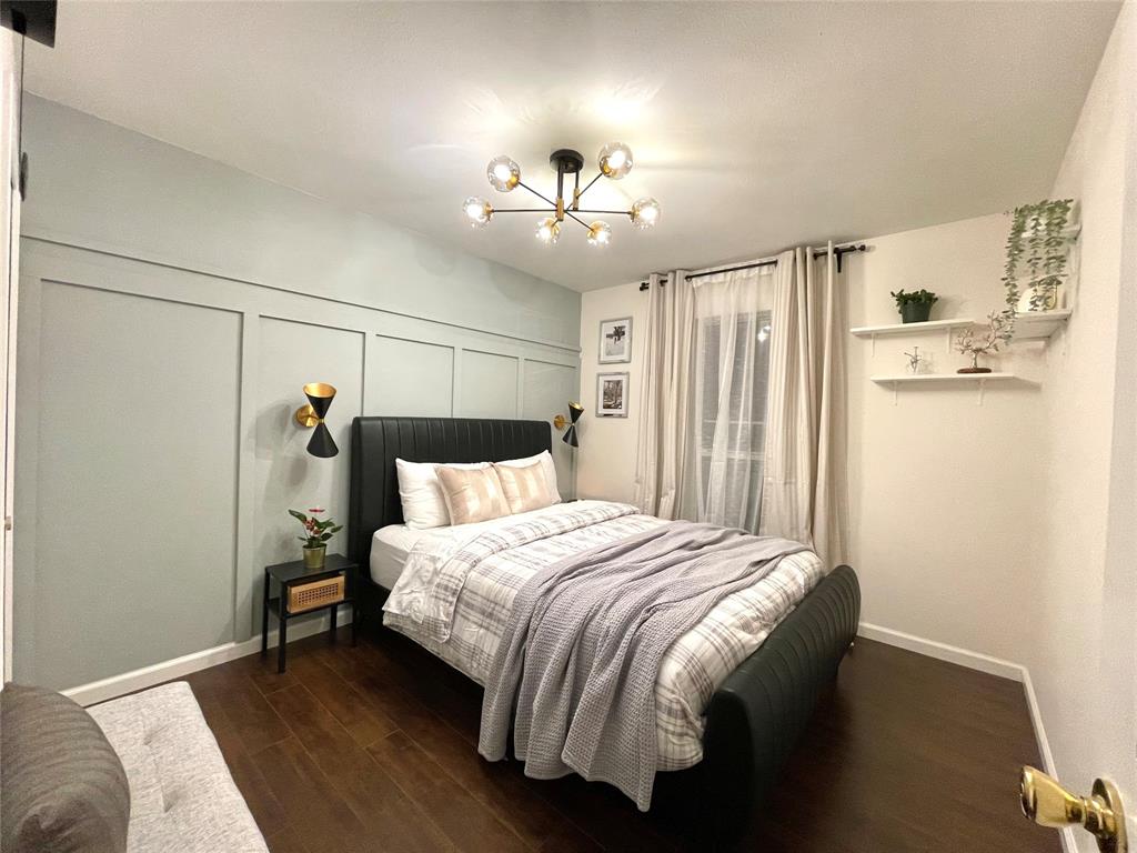 Paneled accent wall, dark wood-finish flooring, multi-arm sputnik ceiling fixture, dual wall-mounted sconces, and built-in floating shelving
