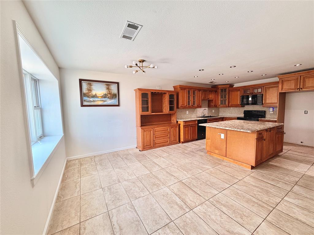 Kitchen featuring wood cabinetry, integrated hutch, center island with stone-finish countertop, recessed lighting, and tile flooring