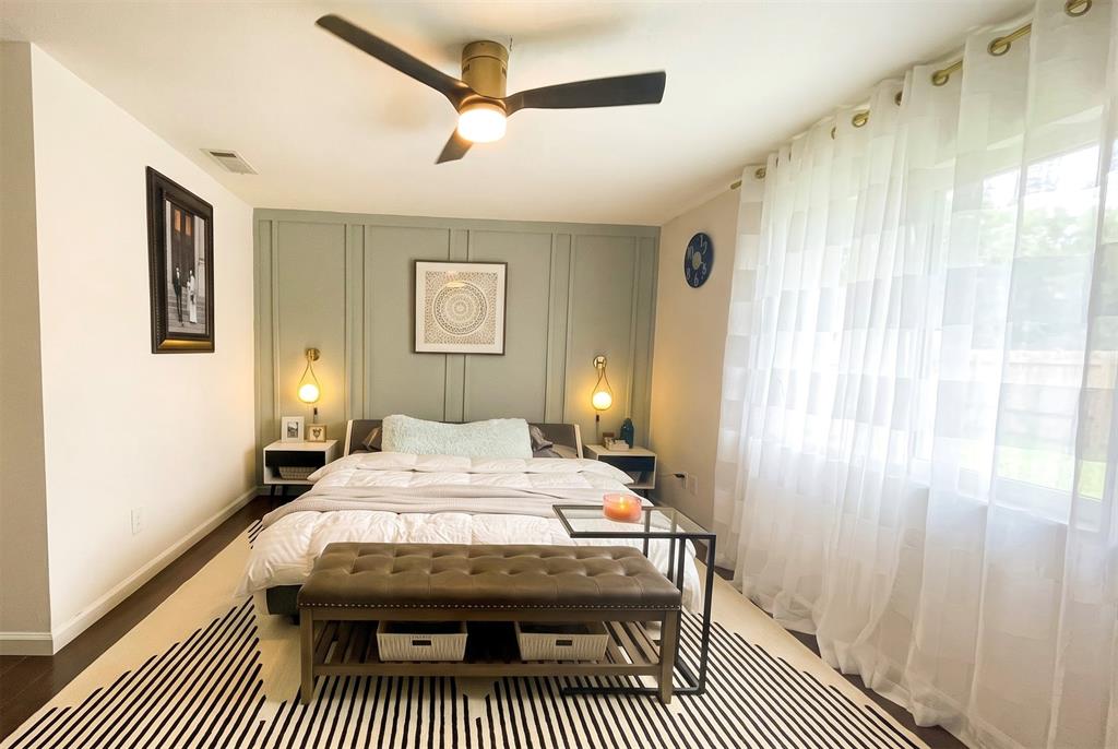 Sage green accent wall with vertical board-and-batten molding, dark wood-finish flooring, brushed gold ceiling fan with integrated lighting, and dual wall-mounted pendant fixtures