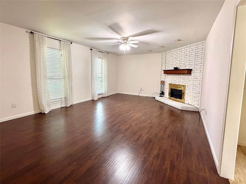 Spacious living area featuring wood-finish flooring, a white-painted brick fireplace, a wooden mantel, and a central ceiling fan