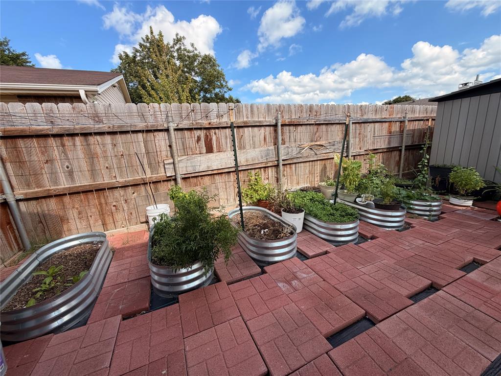 Outdoor space featuring red paver patio flooring, multiple corrugated metal garden beds, and wood privacy fencing