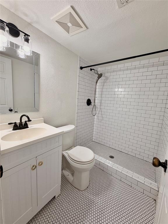 Bathroom featuring a white vanity cabinet with a light-toned countertop, subway tile shower surround, hexagonal tile flooring, and matte black plumbing fixtures