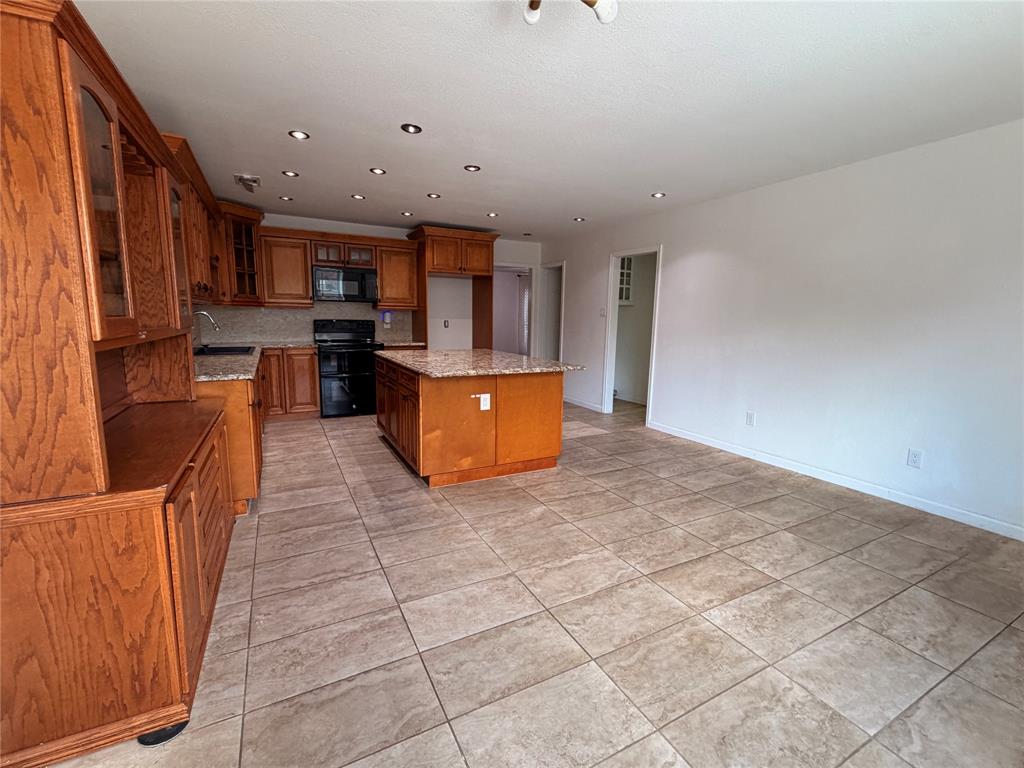 Kitchen featuring medium-tone wood cabinetry, stone-surface countertops, central island, tiled flooring, and recessed ceiling lighting
