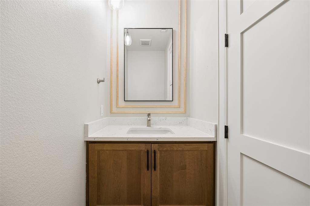 Single-sink vanity featuring wood-finish cabinetry, a white countertop with integrated basin, framed rectangular wall mirror, and matte black hardware