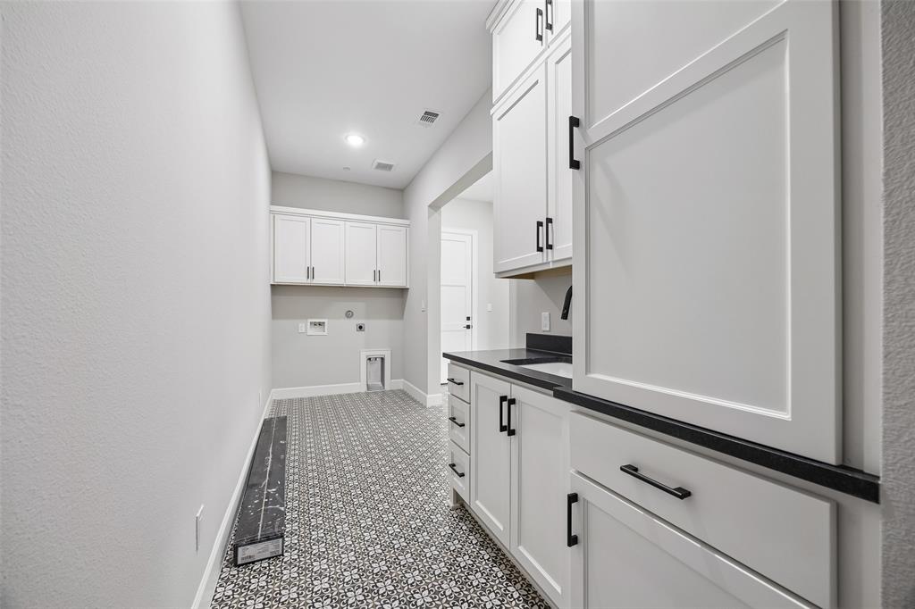 White cabinetry featuring matte black hardware, stone-finish countertops, patterned tile flooring, and integrated wall-mounted cabinetry