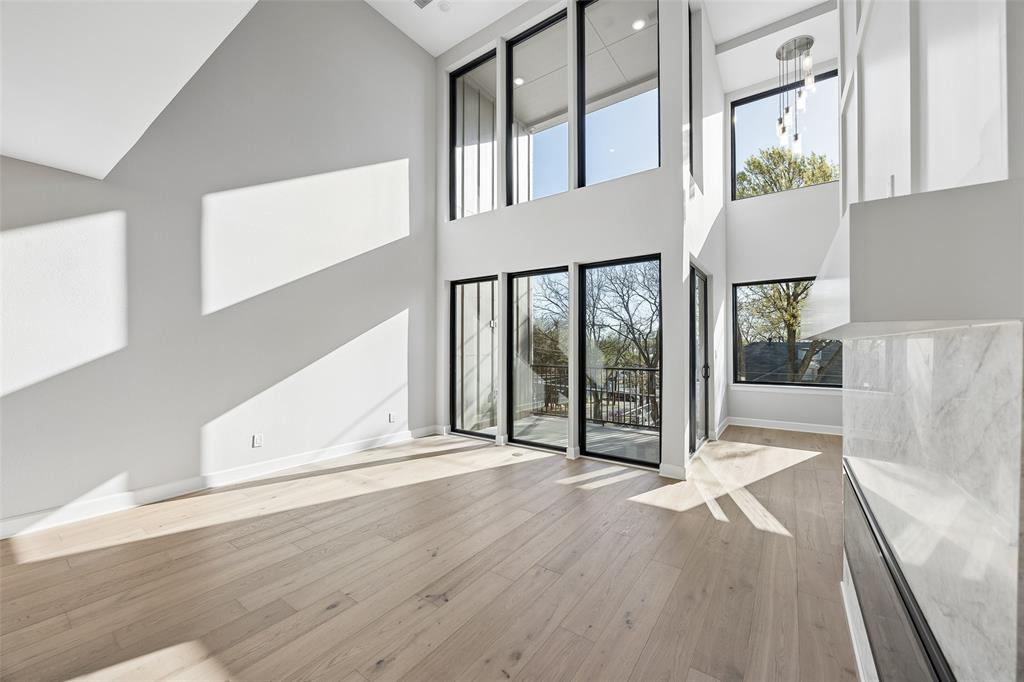 Vaulted ceiling featuring expansive floor-to-ceiling windows with black frames, wood-finish flooring, and a fireplace surround with light-toned stone finish