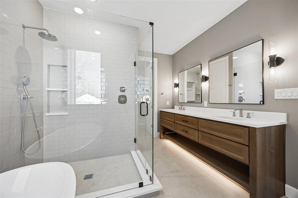 Bathroom featuring a double vanity with a white countertop, glass-enclosed shower with subway tile surround, built-in shower niche, and wall-mounted vanity mirrors