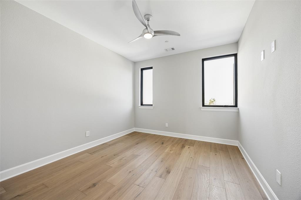 Room featuring wood-finish flooring, a modern three-blade ceiling fan, and windows framed in black
