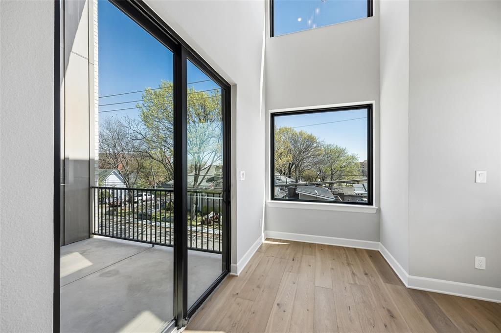 Double-height space featuring floor-to-ceiling black-trimmed windows, wood-finish flooring, and a covered balcony with a metal railing