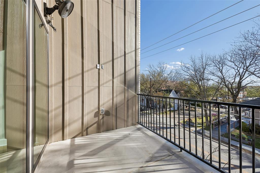 Covered balcony featuring vertical board siding, concrete flooring, black metal railing, and an exterior wall-mounted light fixture