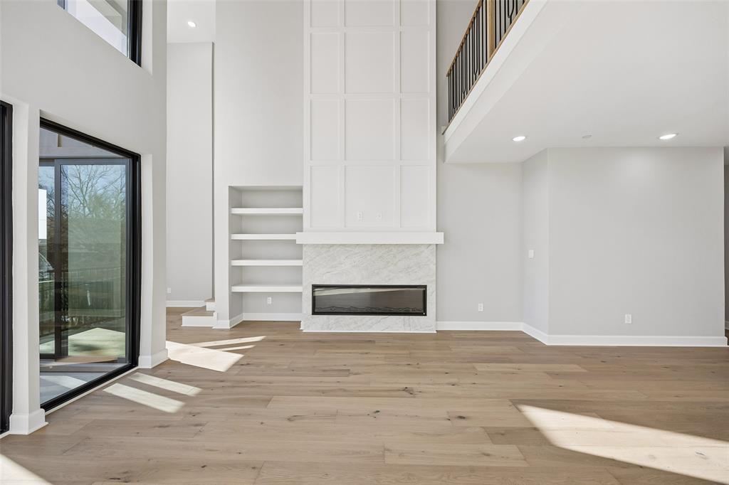 Double-height ceiling featuring wood-finish flooring, a floor-to-ceiling fireplace with stone surround, custom built-in shelving, and metal staircase railing