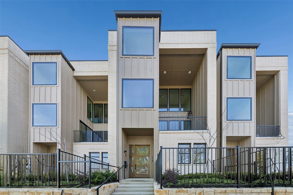 Modern multi-level exterior featuring vertical board-and-batten siding, light-toned masonry, recessed balconies with metal railings, and large fixed-pane windows