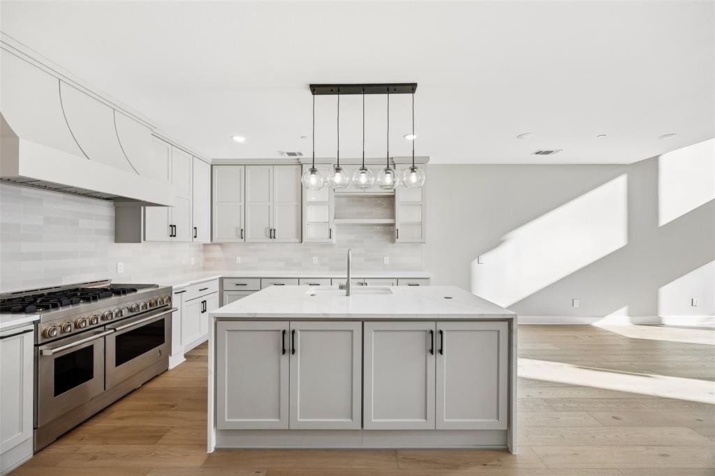 Kitchen featuring light-toned cabinetry, an expansive center island with countertop seating space, a professional-grade stainless steel range with a custom hood, linear tile backsplash, and wood-finish flooring