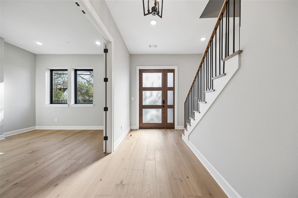 Foyer featuring wood-finish flooring, a multi-panel wood door with glass inserts, and a staircase with matte black metal balusters and a wood handrail